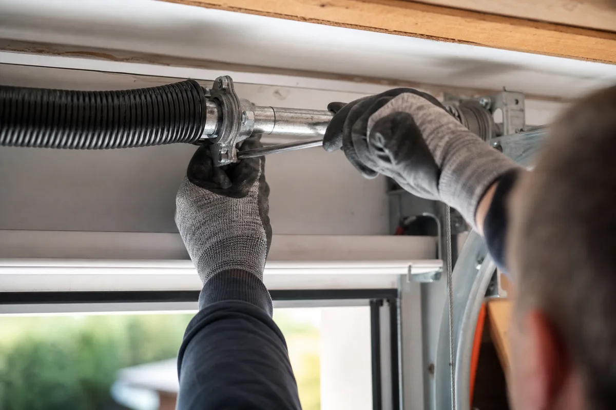 Mains d’artisan réglant le ressort de torsion d’une porte de garage sectionnelle